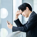 携帯を見ながら悩むサラリーマン男性
