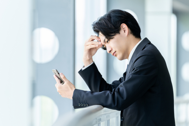 スマホを見ながら悩む会社員の男性